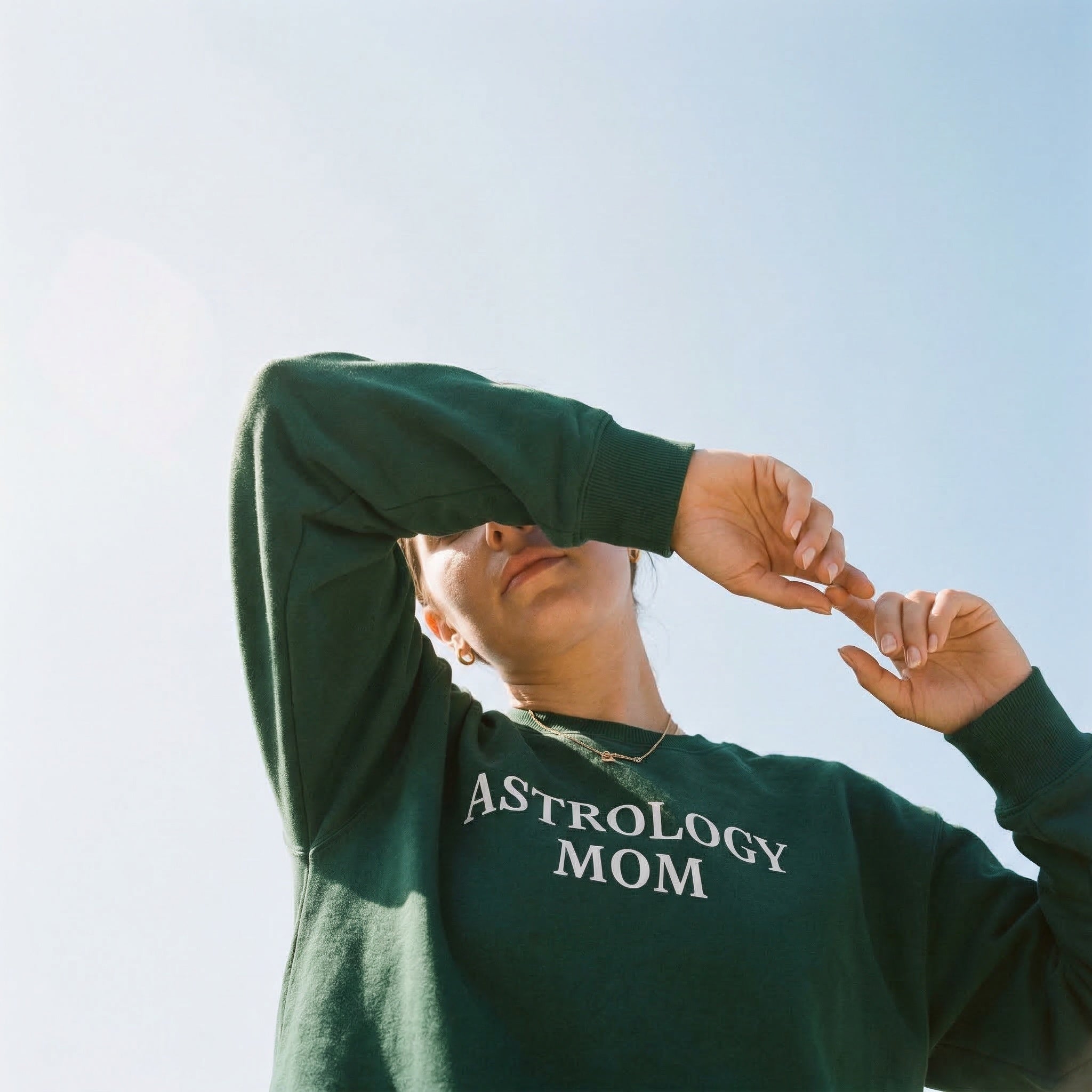 Person wearing a green sweatshirt with 'ASTROLOGY MOM' text against a clear sky.